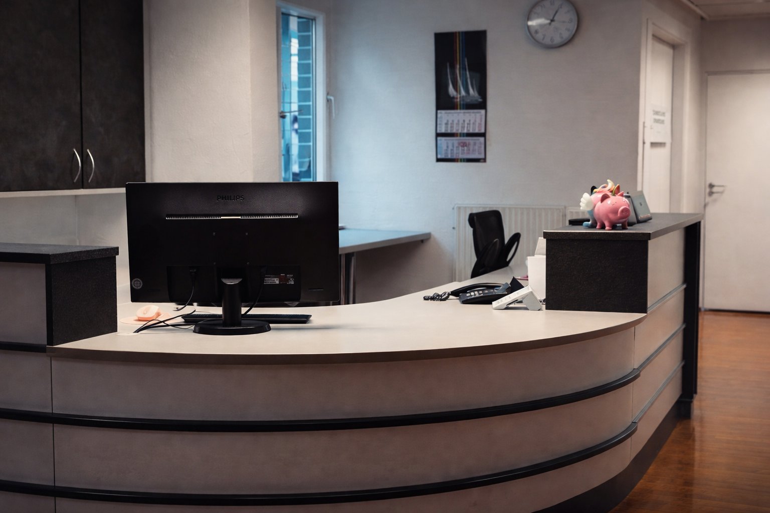 Empfangstresen einer Arztpraxis mit Computer, Telefon und dekorativem Sparschwein im Wartebereich.